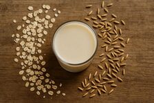 Glas mit Haferdrink, daneben Haferflocken und -körner