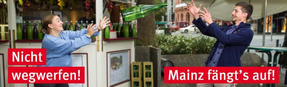 Eine junge Frau wirft eine Weinflasche, ein junger Mann fängt sie auf